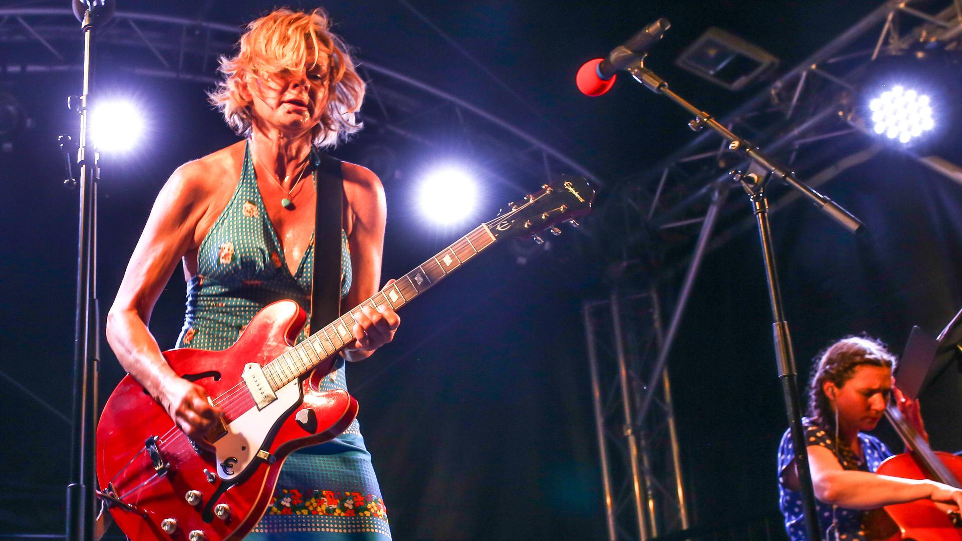 Das Foto zeigt Bernadette La Hengst im engen Kleid und mit breiter roter E-Gitarre in Aktion auf der Bühne. Das Foto zeigt Bernadette La Hengst im engen Kleid und mit breiter roter E-Gitarre in Aktion auf der Bühne.