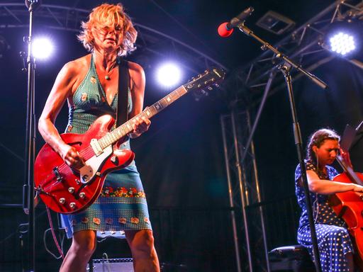 Das Foto zeigt Bernadette La Hengst im engen Kleid und mit breiter roter E-Gitarre in Aktion auf der Bühne. 
