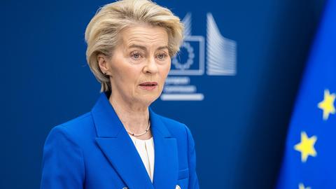 EU-Kommissionspräsidentin Ursula von der Leyen steht in EU-blauem Sakko neben der EU-Flagge an einem Rednerpult. Sie verkündet mit entschlossender Miene den 5-Punkte-Plan zur Wiederaufrüstung Europas.