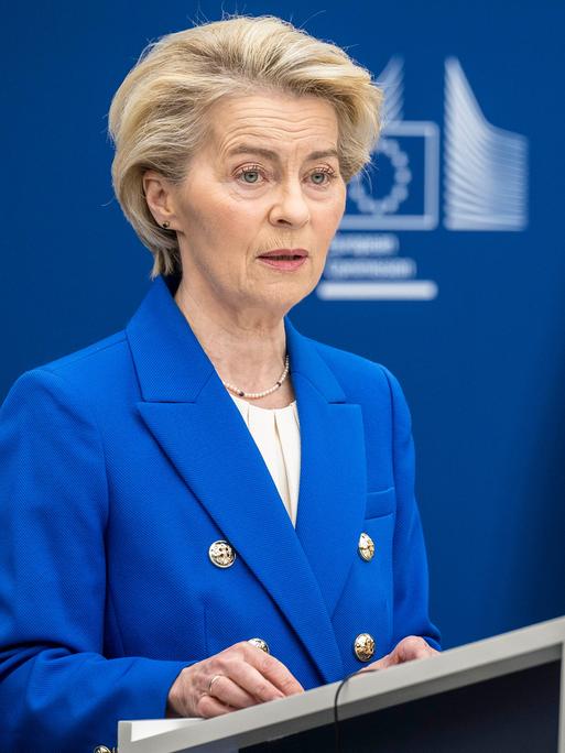 EU-Kommissionspräsidentin Ursula von der Leyen steht in EU-blauem Sakko neben der EU-Flagge an einem Rednerpult