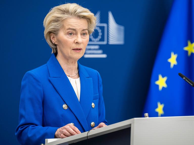 EU-Kommissionspräsidentin Ursula von der Leyen steht in EU-blauem Sakko neben der EU-Flagge an einem Rednerpult