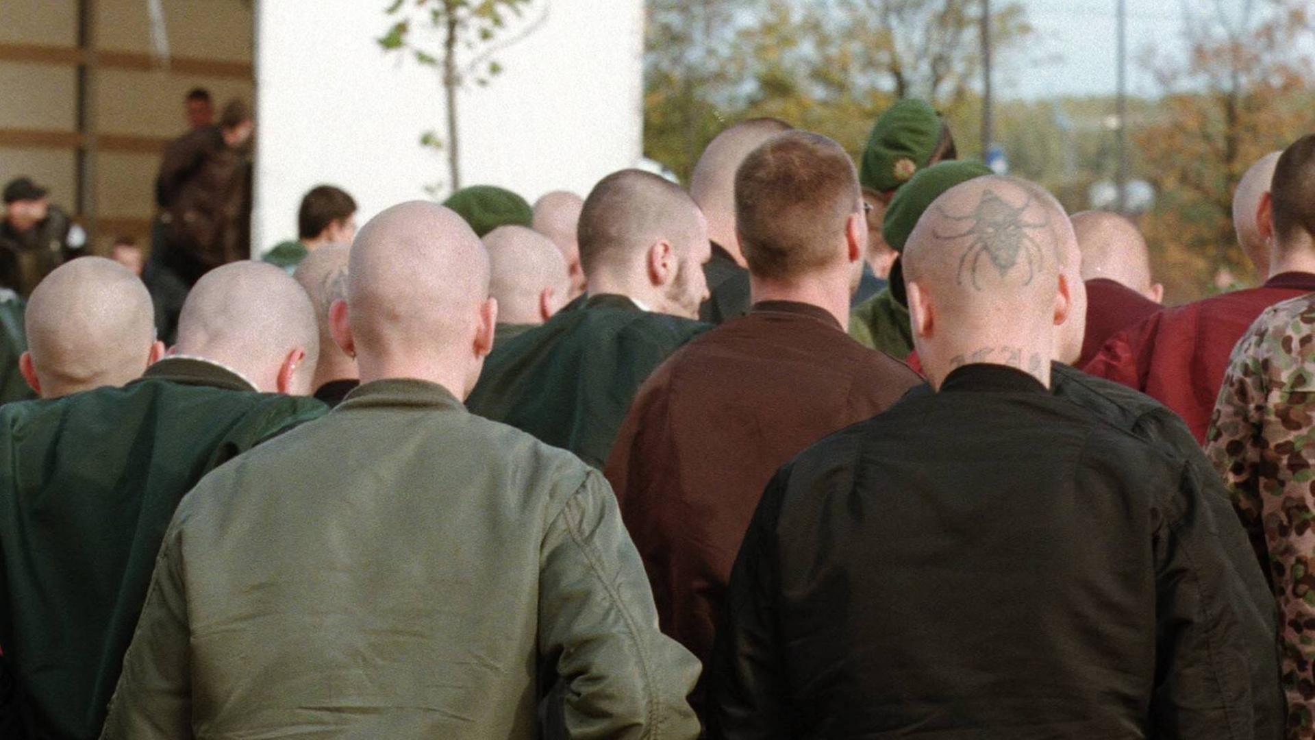 Männer mit Glatzen und in Bomberjacken sind von hinten auf einer Demonstration zu sehen.