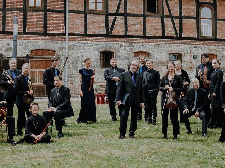Musikerinnen und Sänger stehen auf einer Wiese vor einem historischen Gebäude.