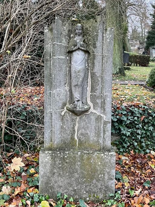 Ein alter Grabstein auf einem Friedhof. Darum Efeu und gefallenes Laub.