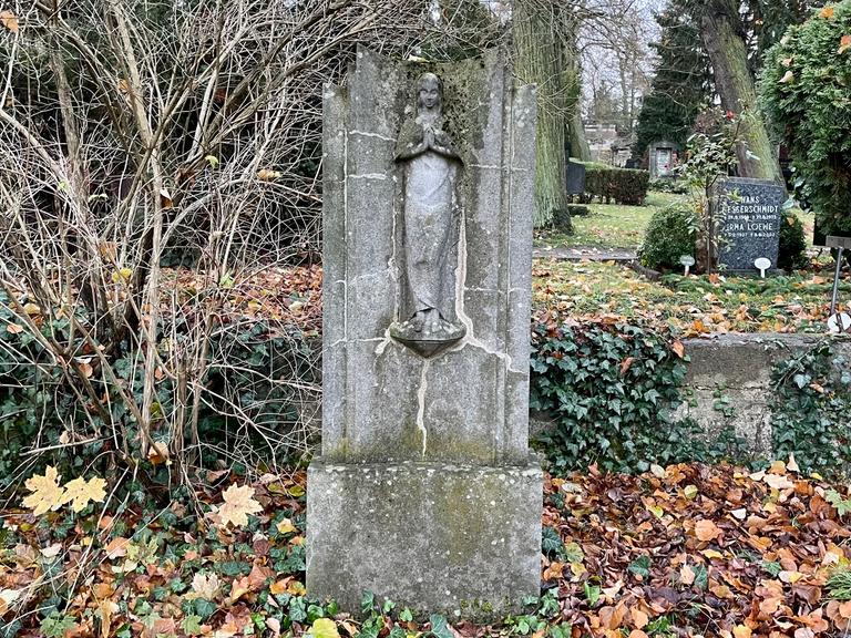 Ein alter Grabstein auf einem Friedhof. Darum Efeu und gefallenes Laub.