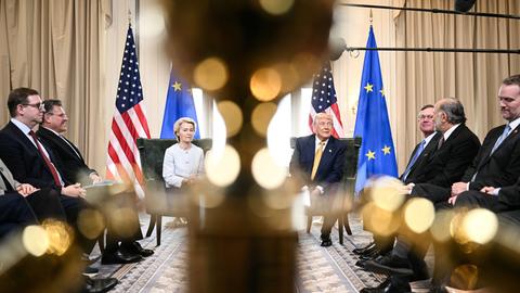 Ursula von der Leyen und Donald Trump sitzen bei einer Pressekonferenz nebeneinander vor US- und EU-Flaggen.