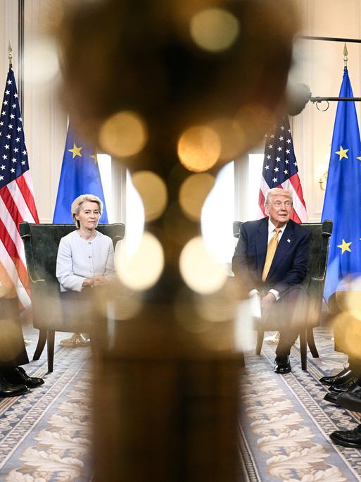 Ursula von der Leyen und Donald Trump sitzen bei einer Pressekonferenz nebeneinander vor US- und EU-Flaggen. Ursula von der Leyen und Donald Trump sitzen bei einer Pressekonferenz nebeneinander vor US- und EU-Flaggen.