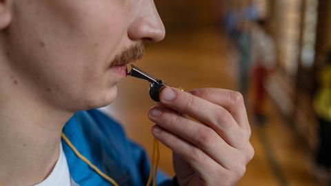 Eine Person führt eine Trillerpfeife an ihren Mund.