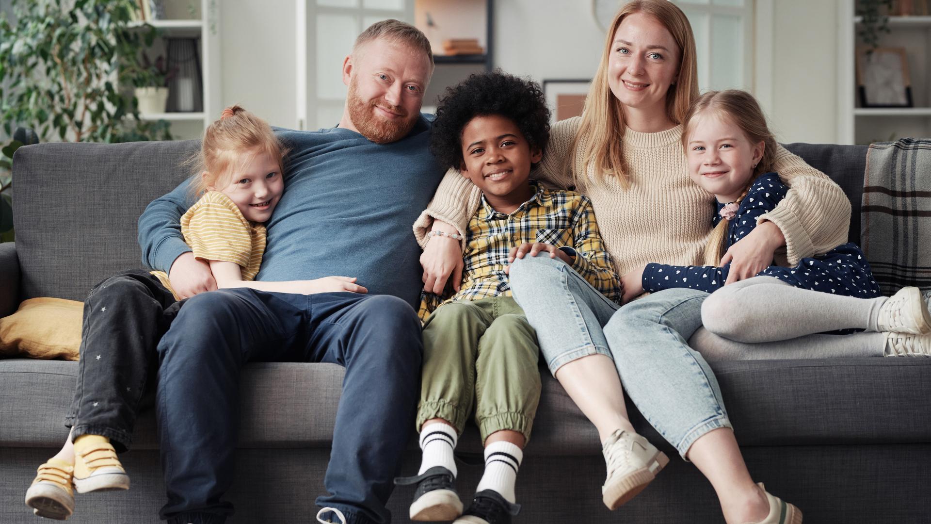 Eine Familie sitzt gutgelaunt zusammen auf dem Sofa, Mutter, Vater und drei Kinder