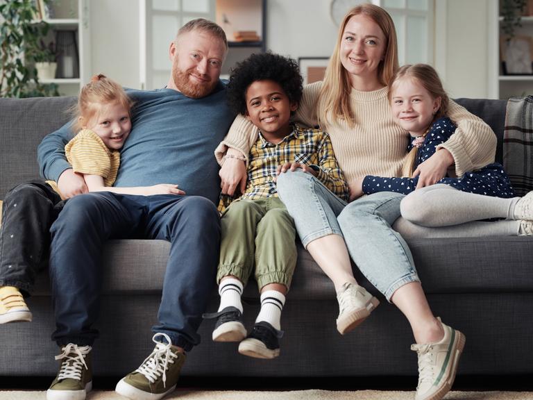 Eine Familie sitzt gutgelaunt zusammen auf dem Sofa, Mutter, Vater und drei Kinder