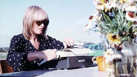 Alice Schwarzer sitzt an einer Schreibmaschine an einem Tisch mit einem Blumenstrauß darauf


