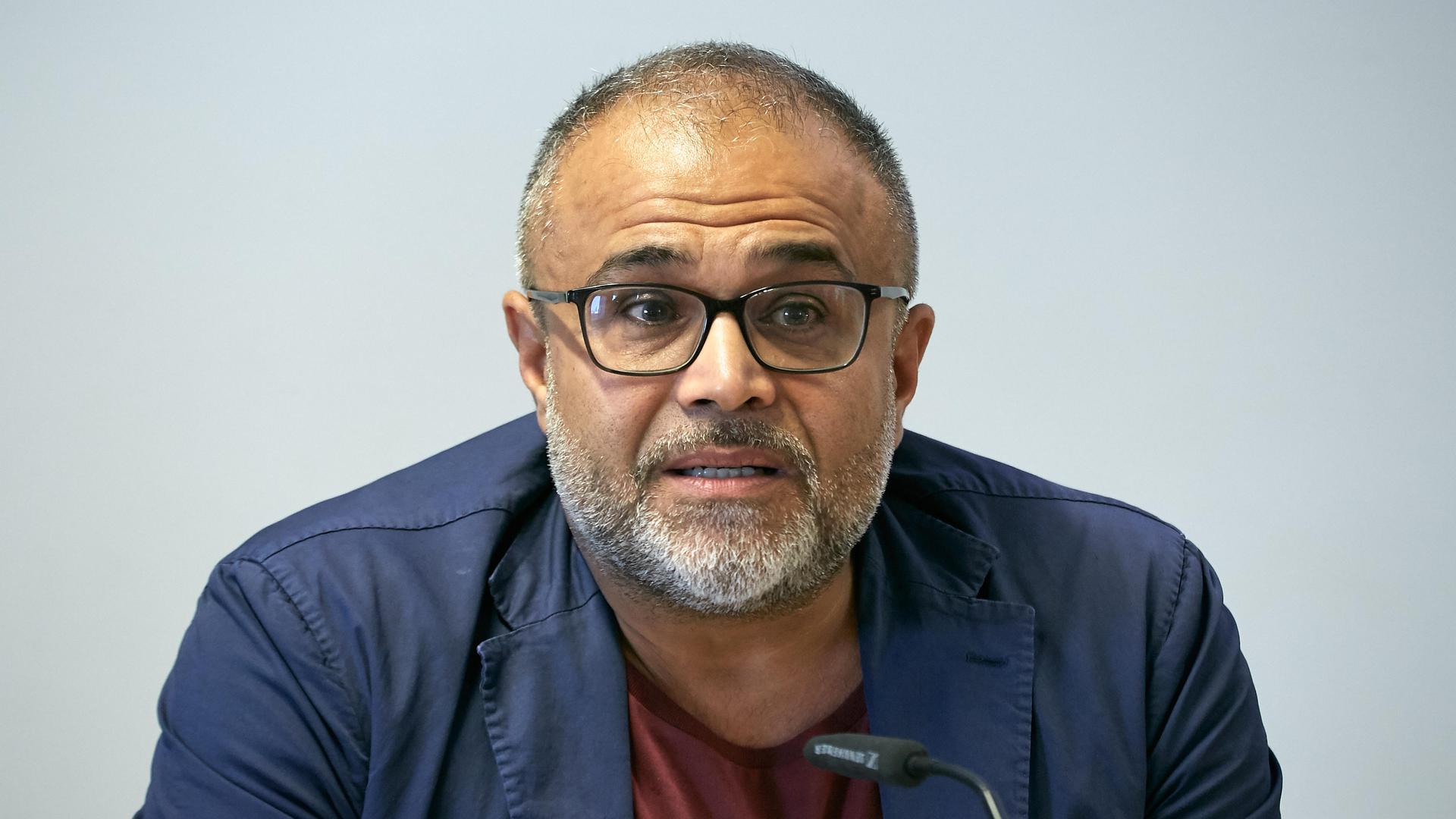 Porträtaufnahme von Ali Ertan Toprak, der hinter einem Mikrofon sitzen.
