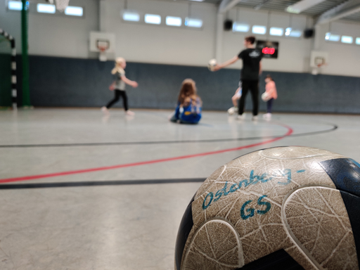 Grundschulkinder beim Fußballspielen in der Halle, im Vordergrund ein Ball