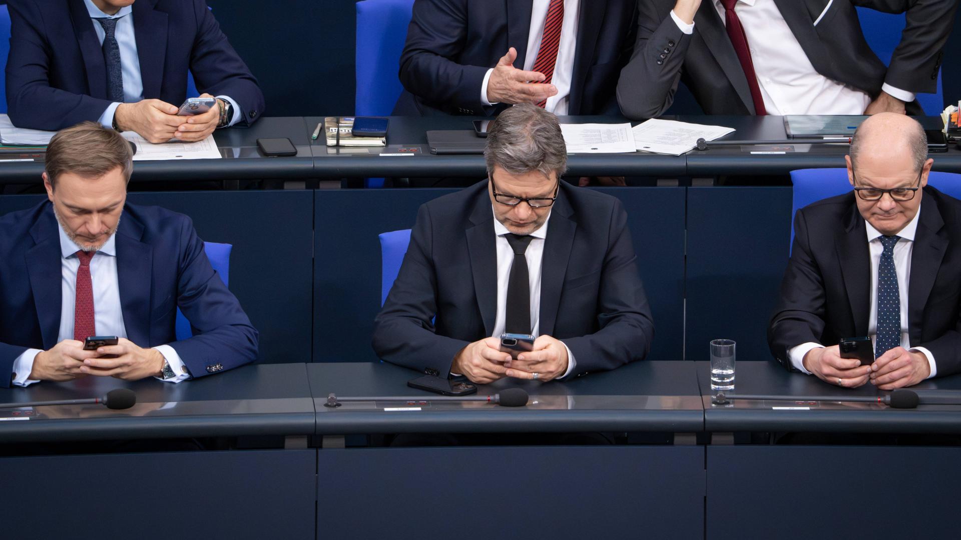 Christian Lindner, Robert Habeck und Olaf Scholz sitzen auf der Regierungsbank im Deutschen Bundestag und blicken in ihre Handys.