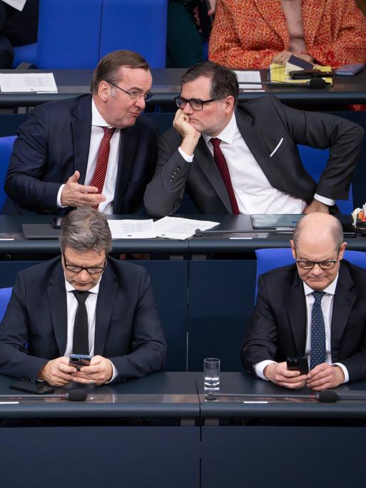 Christian Lindner, Robert Habeck und Olaf Scholz sitzen auf der Regierungsbank im Deutschen Bundestag und blicken in ihre Handys.