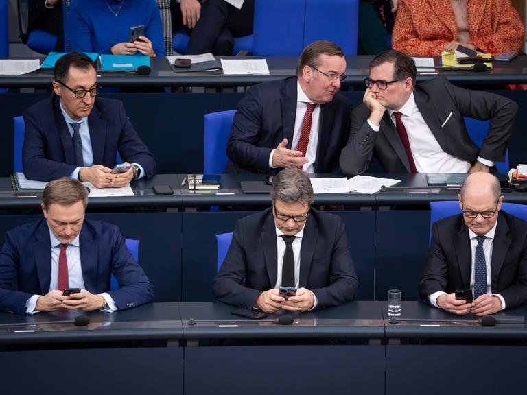 Christian Lindner, Robert Habeck und Olaf Scholz sitzen auf der Regierungsbank im Deutschen Bundestag und blicken in ihre Handys.