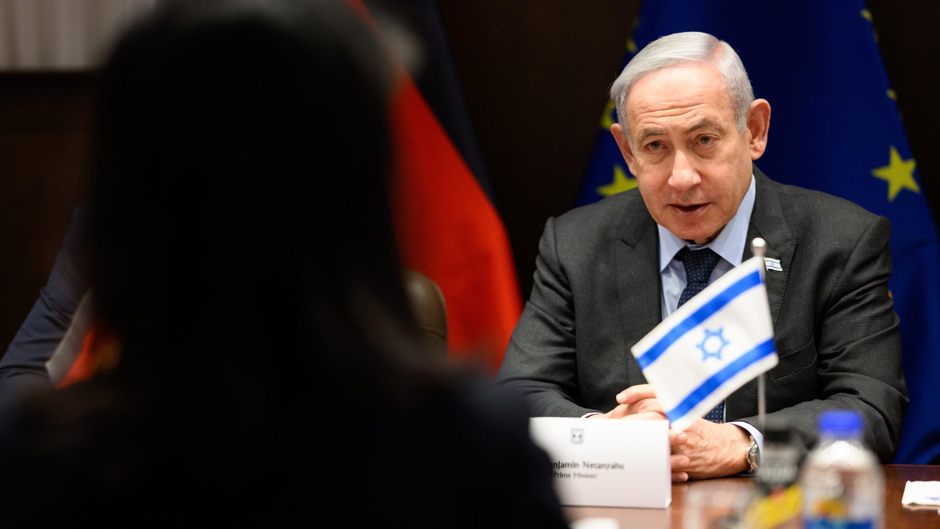 Benjamin Netanjahu, Ministerpräsident von Israel, sitzt an einem Tisch und hört zu, im Vordergrund sieht an den Schatten einer Person, die ihm gegenübersitzt.