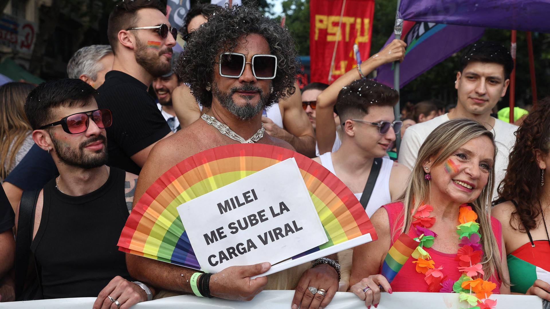 Teilnehmer der Pride-Parade 2025 in Buenos Aires. Ein Mann hält einen Fächer in Regenbogenfarben und ein Schild mit der Aufschrift "Milei me sube la carga viral".