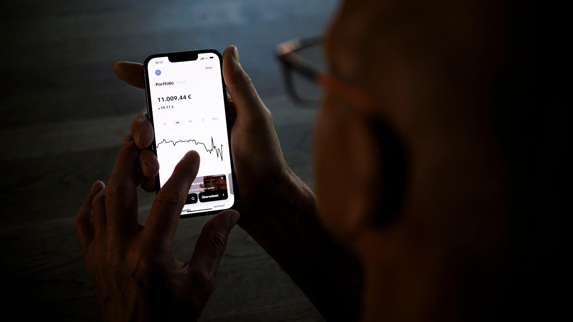 Ein Mann hält ein Smartphone mit einer geöffneten Trading-App und prüft den Aktienkurs seiner Geldanlage. Ein Mann hält ein Smartphone mit einer geöffneten Trading-App und prüft den Aktienkurs seiner Geldanlage.