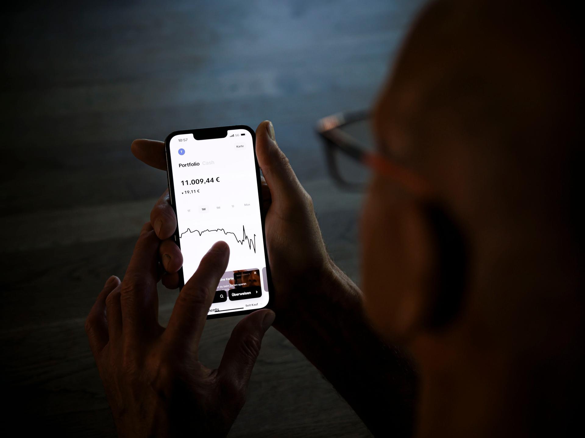 Ein Mann hält ein Smartphone mit einer geöffneten Trading-App und prüft den Aktienkurs seiner Geldanlage.