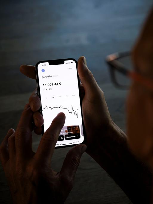 Ein Mann hält ein Smartphone mit einer geöffneten Trading-App und prüft den Aktienkurs seiner Geldanlage.