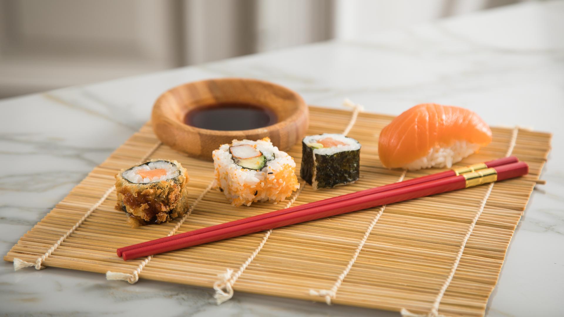 Verschiedene Sushi-Varianten auf einer Sushimatte angerichtet. 