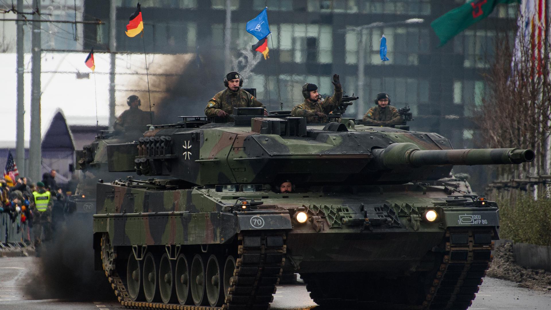 Kampfpanzer vom Typ Leopard 2A6 der deutschen Bundeswehr nehmen an einer Militärparade anlässlich des Tages der Streitkräfte in Vilnius teil, deutsche und NATO Flaggen wehen auf dem Panzer, ein Soldat winkt