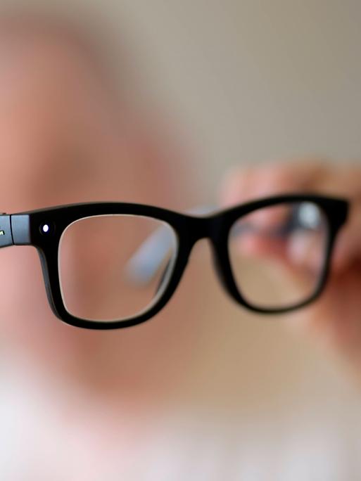 Eine schwarze KI Brille in der Hand eines Menschen