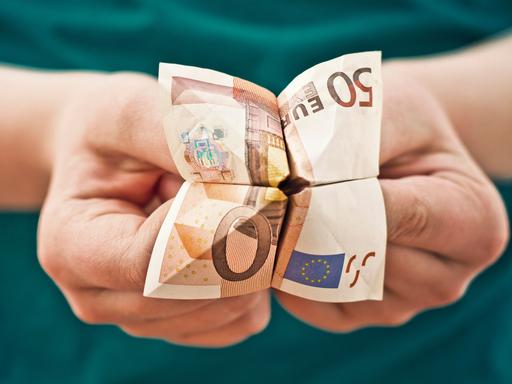 Kinderhände, die einen aus einem 50-Euro-Schein gebastelten Papier-Wahrsager halten.
