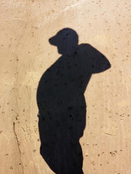 Schatten eines dicken Mannes am Sandstrand.