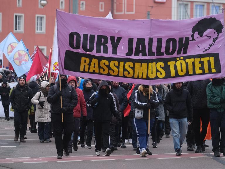 Teilnehmer einer linken Demonstration gehen mit Transparenten und Fahnen durch die Stadt Dessau. Anlass ist der 19. Todestag des Asylbewerbers Oury Jalloh, der am 07. Januar 2005 in einer Polizeizelle ums Leben kam.