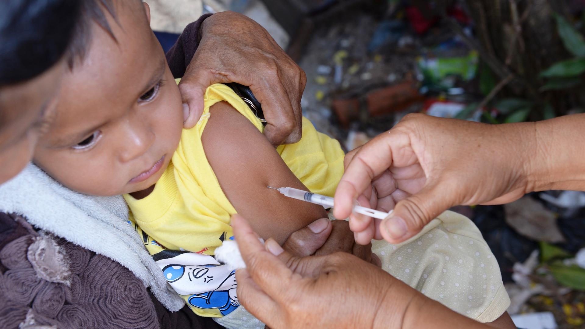 Ein Kind sitzt auf dem Arm seiner Mutter. Es bekommt mit einer Nadel eine Impfung in seinen Arm.