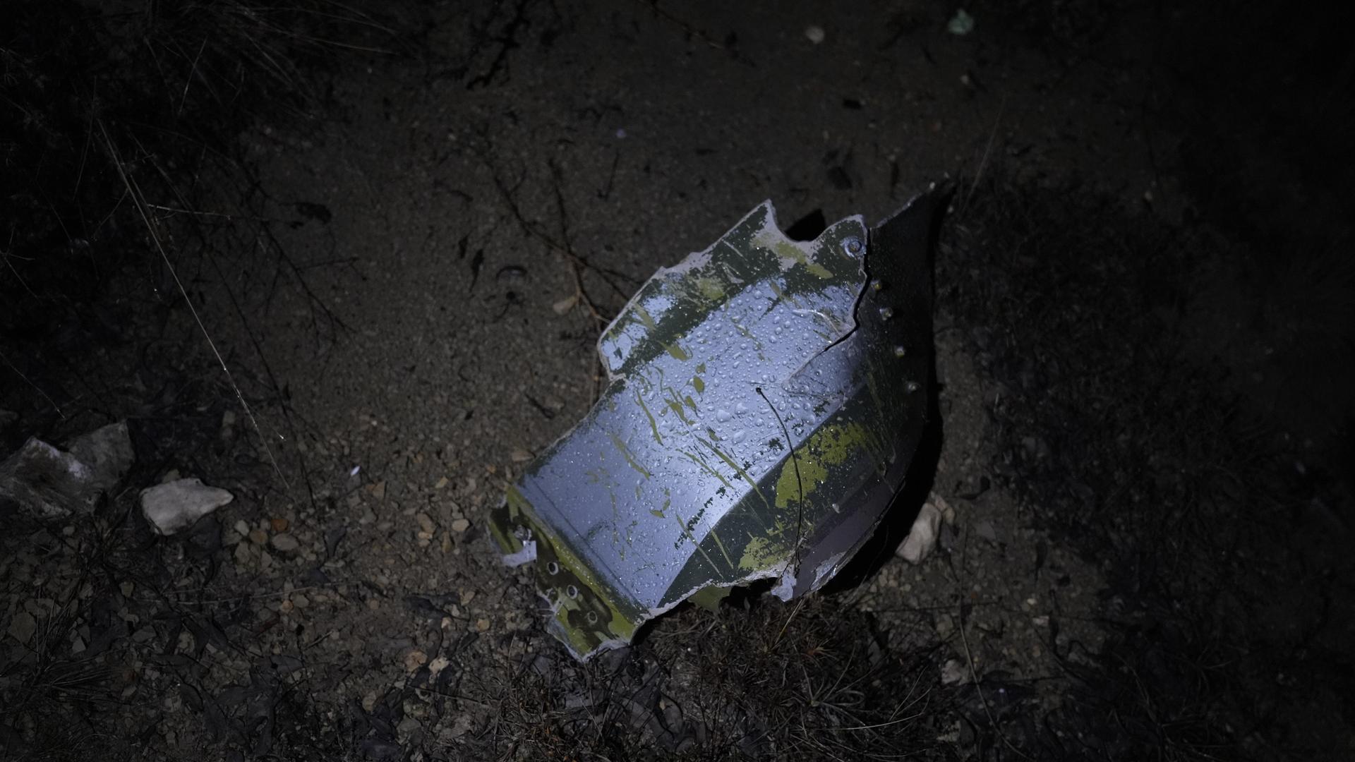 Ein metallenes Trümmerteil auf matschigem Boden wird von einer Lampe angestrahlt.