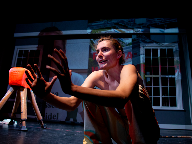 Eine Frau sitzt auf einer Bühne. Sie hat die Hände vor sich gehalten. Es ist die Schauspielerin Anna K. Seidel in der Inszenierung von Woyzeck.