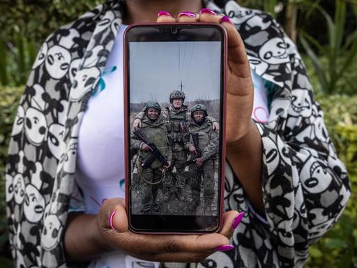 Grace Gathoni Kagombe hält ein Foto ihres Mannes Martin Macharia Mburu (links) in Militäruniform in den Händen. Den Berichten zufolge starb er im Krieg Russlands gegen die Ukraine im Einsatz für Russland.