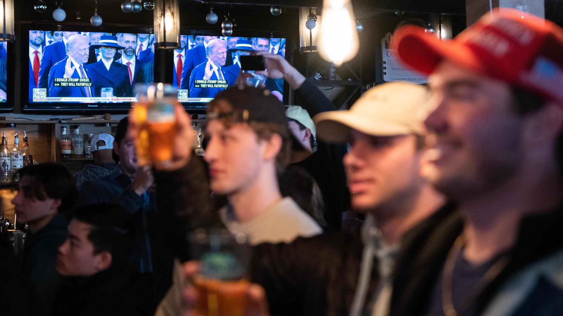 Junge Männer mit Getränken in den Händen schauen während einer Party die Inauguration von Donald Trump.