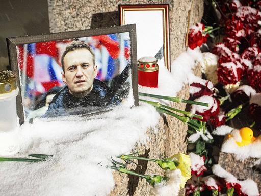 Ein Bild von Alexej Nawalny steht auf einer Mauer. Daneben liegen Blumen.