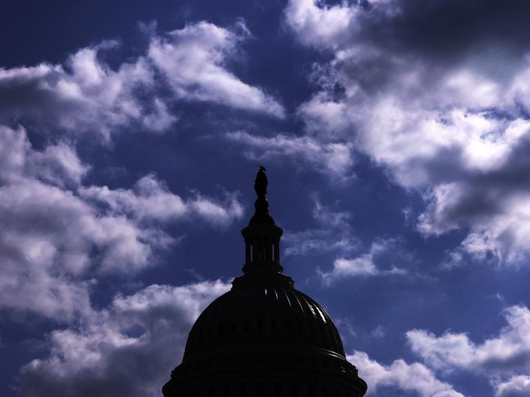 Das Dach des Kapitols in Washington hebt sich dunkel vor einem bewölkten Himmel ab.