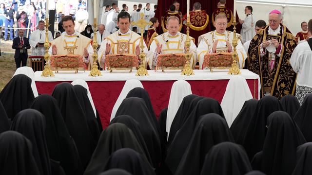 Vier Männer in hellen Kirchen-Kleidern beten. Vor ihnen sind viele Frauen mit schwarzen Kopf-Tüchern zu sehen.