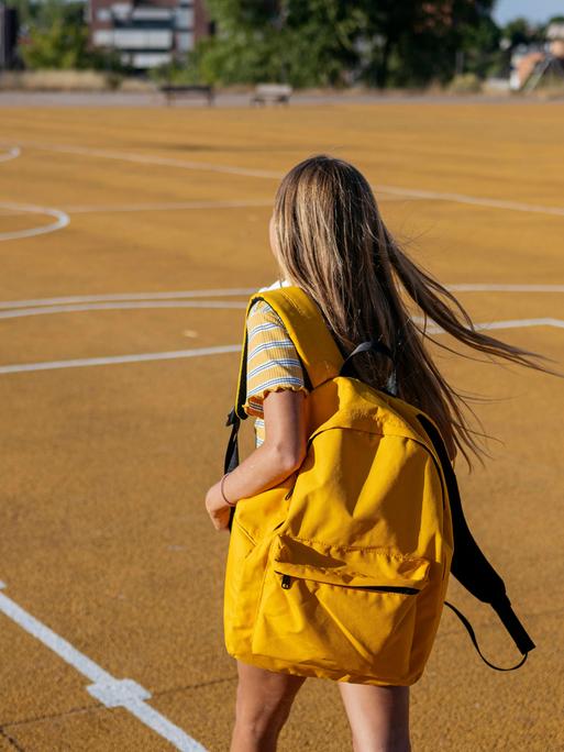 Ein junges Mädchen trägt einen Rucksack und geht über einen Basketballplatz.
