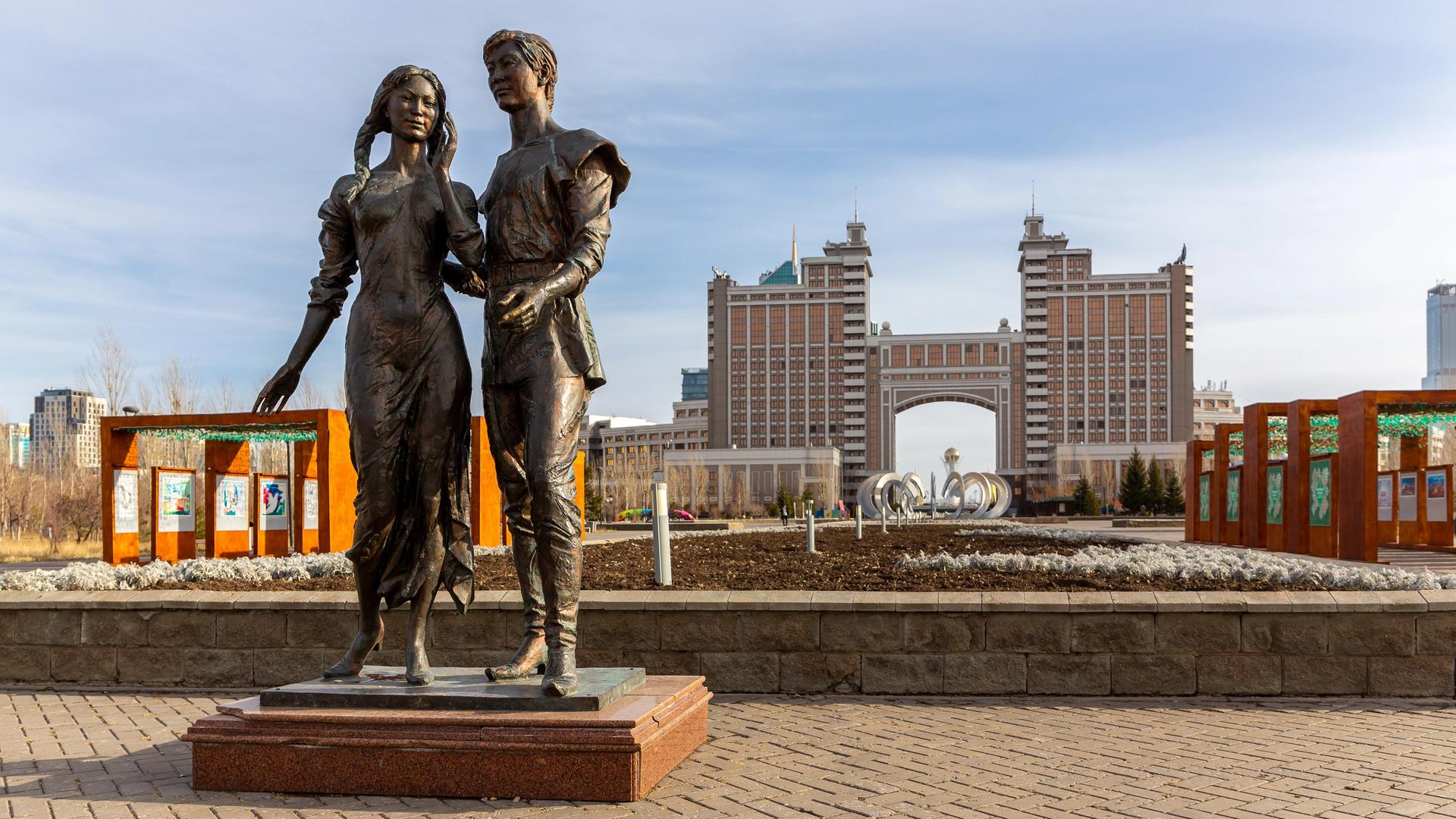 Bronzeskulptur von Mann und Frau im Park der Liebenden in Astana mit der Skyline der Stadt im Hintergrund, Kasachstan, 2022.