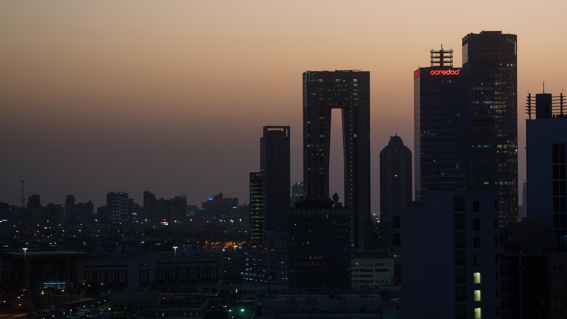 Das Foto zeigt die Skyline von Kuwait-City. Der Himmel ist wegen der aufgehenden Sonne rötlich gefärbt.