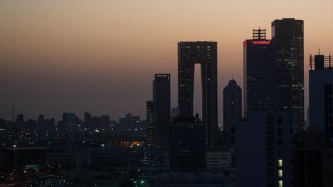 Das Foto zeigt die Skyline von Kuwait-City. Der Himmel ist wegen der aufgehenden Sonne rötlich gefärbt.