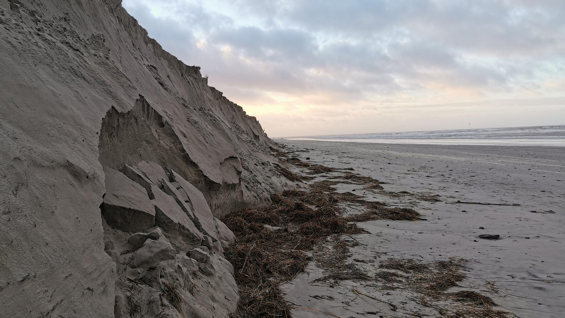 Eine Abbruchkante im Sand, dahinter Strand und das Meer Eine Abbruchkante im Sand, dahinter Strand und das Meer