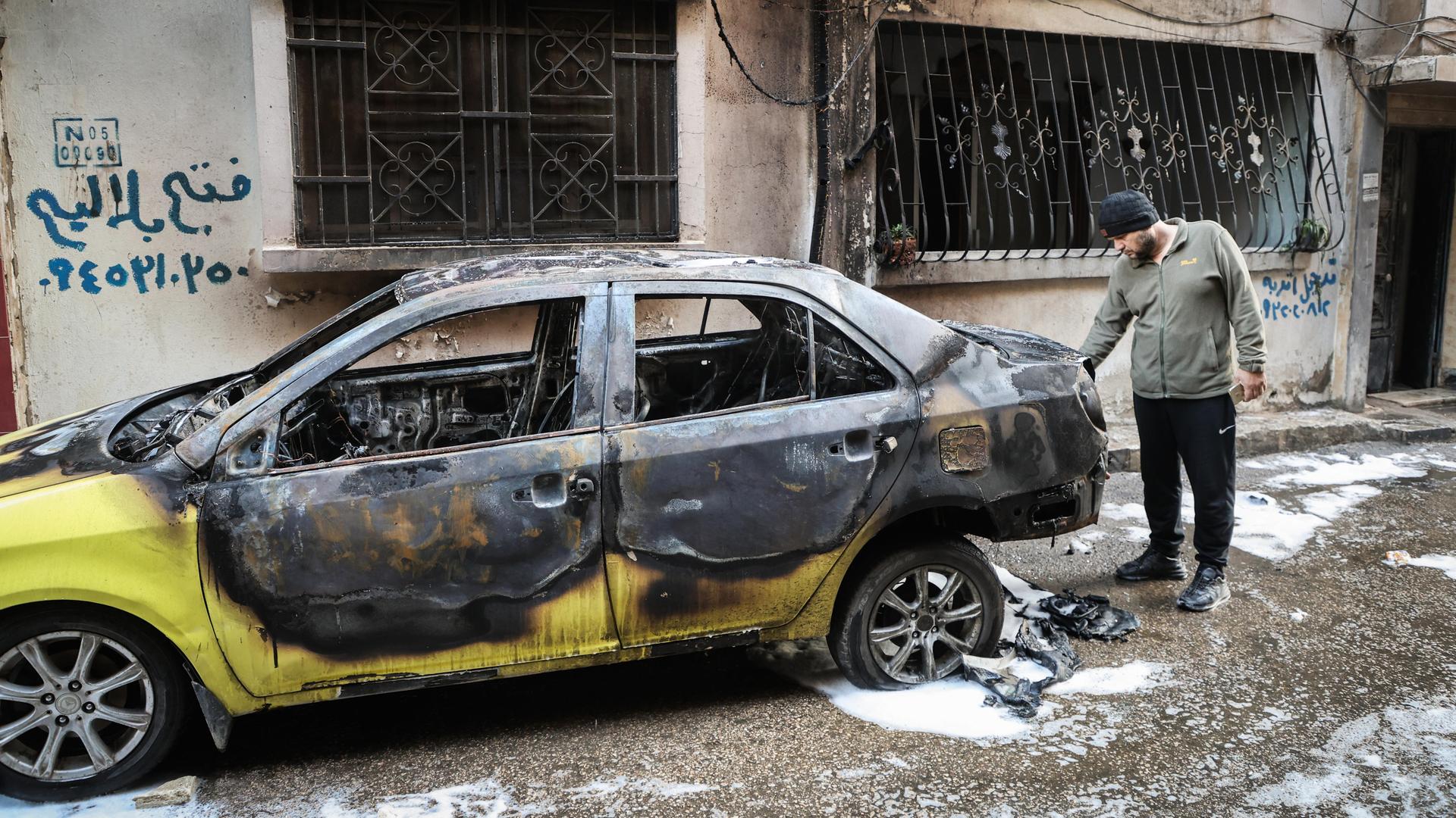 Eine Person steht hinter einem ausgebrannten Fahrzeug. Eine Person steht hinter einem ausgebrannten Fahrzeug.