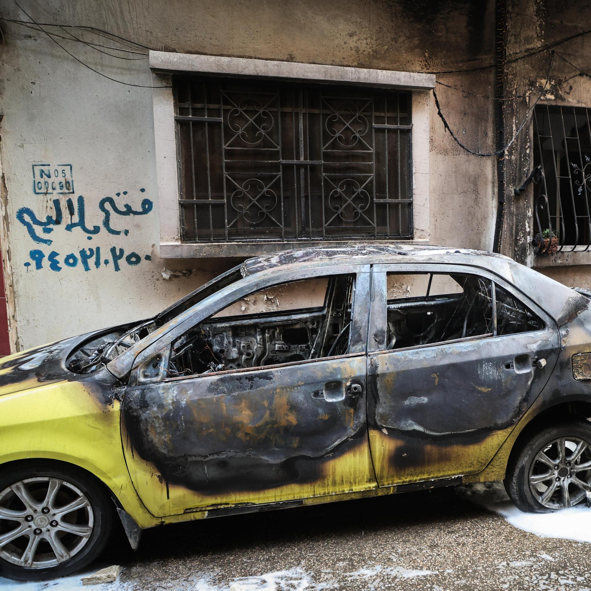 Eine Person steht hinter einem ausgebrannten Fahrzeug. 