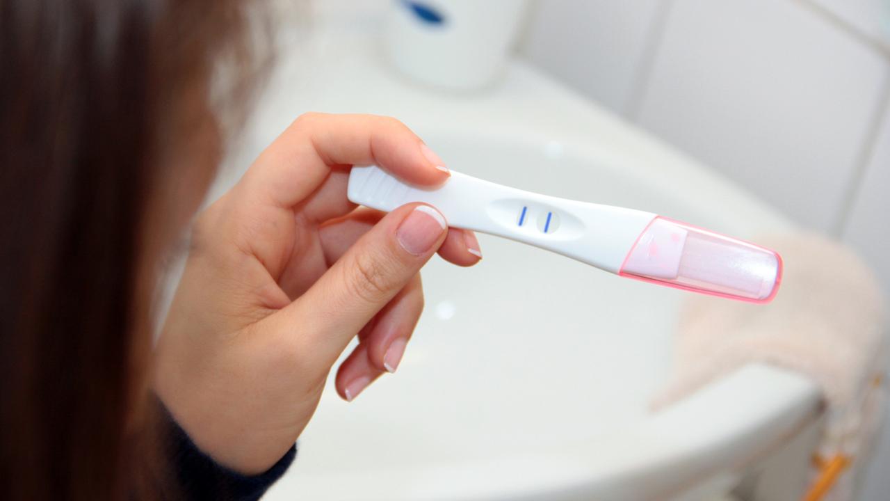 Eine Frau blickt auf einen positiven Schwangerschaftstest. Eine Frau blickt auf einen positiven Schwangerschaftstest.