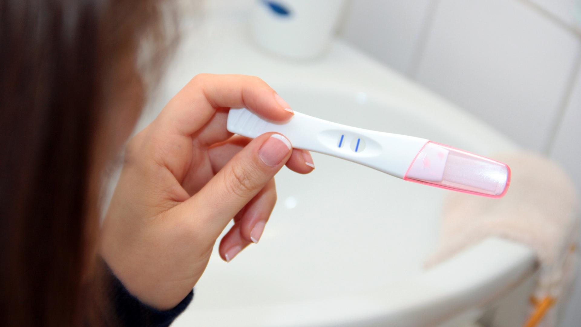 Eine Frau blickt auf einen positiven Schwangerschaftstest.