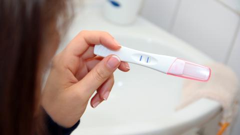 Eine Frau blickt auf einen positiven Schwangerschaftstest. Eine Frau blickt auf einen positiven Schwangerschaftstest.