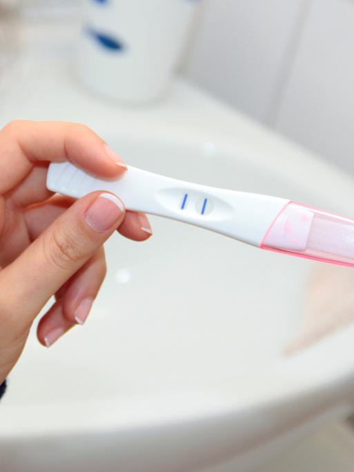 Eine Frau blickt auf einen positiven Schwangerschaftstest.